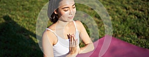 Portrait of young mindful woman, practice yoga, exercising, inhale and exhale on fresh air in park, sitting on rubber