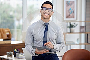 Portrait of a young mixed race businessman holding and using a digital tablet standing in an office at work. One content