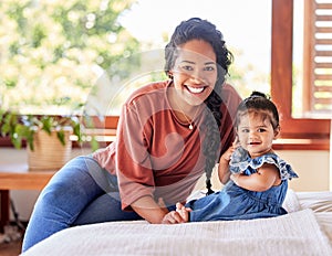 Portrait of young mixed race mother sitting with her adorable baby girl on the bed in a bedroom at home. Hispanic woman