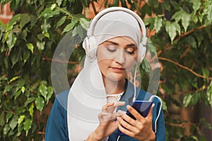 Portrait of young modern arabian woman holding mobile phone and listening the music to headphone.