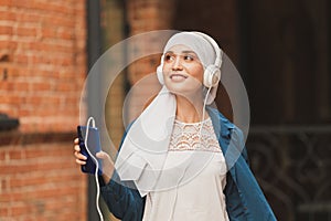 Portrait of young modern arabian woman holding mobile phone and listening the music to headphone.