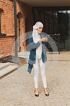 Portrait of young modern arabian woman holding mobile phone and listening the music to headphone.