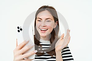 Portrait of young modern girl connects to video chats, talks with friend online using smartphone app, waves at mobile