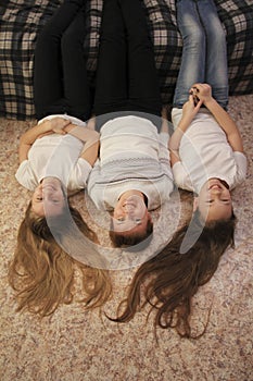 Portrait of young mom and her two teen daughters lying on the floor at home, their feet on the couch