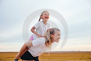 Portrait of young mother carrying her daughter on her back. Happy chilhood