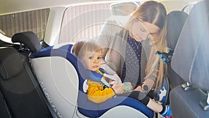 Portrait of young mother fastening belts and bucle of car children safety seat