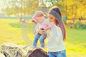 Portrait of young mother helping her little baby to walk outdoors in summer park