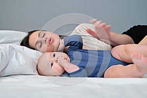 Portrait of young mother and her baby son, parent and baby lying in bed together