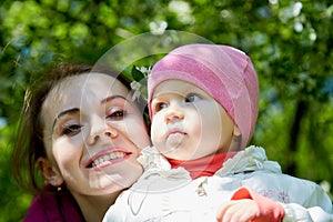 Portrait of young mother and her small daughter in the park full of apple blossom trees in a spring day. Woman and girl in nature