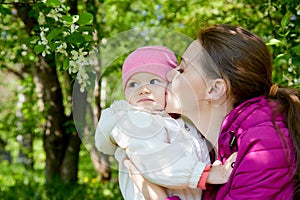 Portrait of young mother and her small daughter in the park full of apple blossom trees in a spring day. Woman and girl in nature