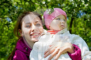 Portrait of young mother and her small daughter in the park full of apple blossom trees in a spring day. Woman and girl in nature