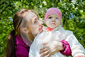 Portrait of young mother and her small daughter in the park full of apple blossom trees in a spring day. Woman and girl in nature