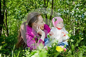 Portrait of young mother and her small daughter in the park full of apple blossom trees in a spring day. Woman and girl in nature