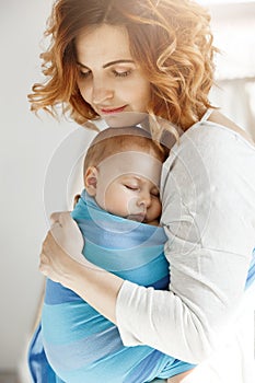 Portrait of young mother and newborn son sleeping on mother chest in blue baby sling. Family happiness vibes. Family