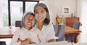 Portrait of a young mother relaxing and using a laptop with her daughter at home. Smiling little girl browsing a pc and
