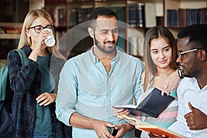 Portrait of young multicultural friends reading books together in the library