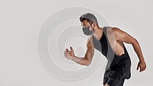 Portrait of young muscular caucasian man wearing black medical mask looking aside while ready to run, standing isolated
