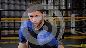 Portrait of a young muscular guy in blue boxing gloves in the gym.