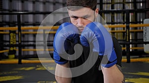 Portrait of a young muscular guy in blue boxing gloves in the gym.