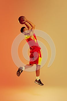 Portrait of young muscular man, basketball player training, playing  over orange studio background in neon light