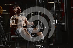 Portrait of young muscular man training shirtless in gym indoors. Pulling rope with weigh. Relief body shape. Concept of