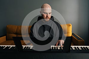 Portrait of young musician male with hoodie and beard playing electric piano or digital keyboard, practicing and photo