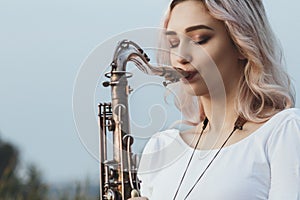Portrait of young musician on nature background, woman face playing saxophone and blowing into the trumpet, concept music and
