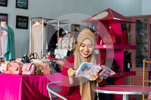 Portrait of a young muslim entrepeneur sitting and reading magazine looking new stock catalog in her fashion boutique