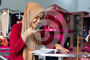 Portrait of a young muslim entrepeneur sitting and reading magazine looking new stock catalog in her fashion boutique