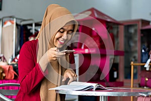 Portrait of a young muslim entrepeneur sitting and reading magazine looking new stock catalog in her fashion boutique