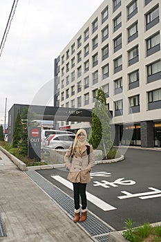 Portrait of young muslim woman smiling and standing on sidewalk at front of hotel