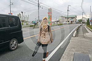 Portrait of young muslim woman wearing hijab smiling and walking on sidewalk with car on road