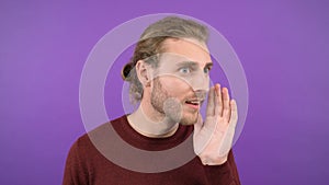 Portrait of a young mysterious long-haired guy who shares a secret while holding his palm over his mouth 4K