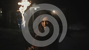 Portrait of a young mystic woman in the dark holding a torch.