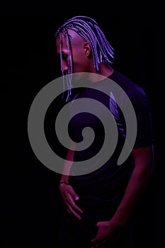 Portrait of a young naked african man at studio. High Fashion male model in colorful neon bright lights posing on black background