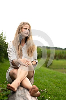 Portrait of young natural woman sitting on wooden log outdoors