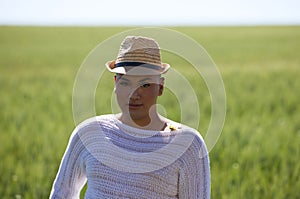 Portrait of a young non-binary latin person wearing a straw hat and standing in the green wheat field making different expressions