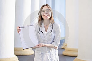 Portrait of a young nurse, medical university student girl stands with phonendoscope and documents, happy female doctor in uniform