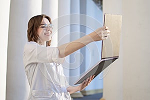 Portrait of a young nurse, a medical university student stands with a phonendoscope and reads a paper, happy female doctor in