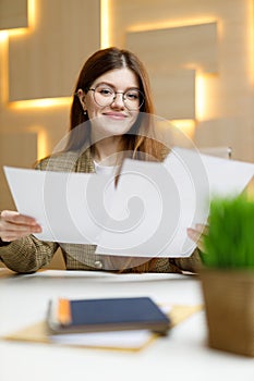 Portrait of a young office staff woman with paper in her hands at the workplace, reports and financial mail