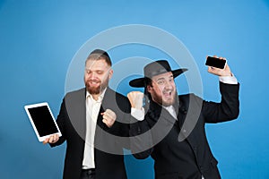 Portrait of a young orthodox jewish men isolated on blue studio background, meeting the Passover, winners