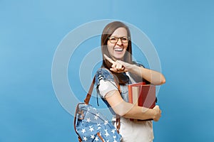 Portrait of young overjoyed laighing woman student in glasses with backpack holding books, pointing index finger on copy