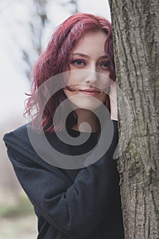 Portrait of young pale woman lean on tree winter day in park