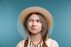 Portrait of a young pensive girl in summer hat isolated over blue background,