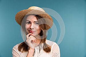 Portrait of a young pensive girl in summer hat isolated over blue background