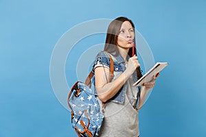 Portrait of young pensive woman student in denim clothes with backpack taking exam thinking about test holding notebook