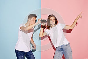 Portrait of young people, man and woman looking in binoculars isolated over blue-pink background. Tourists, travelling