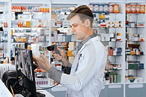 Portrait of young pharmacist scanning barcode of mockup qualified pill bottle.