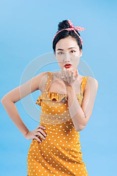 Portrait of young pin-up woman 20s in vintage polka dot dress smiling and flirting at camera isolated over blue background