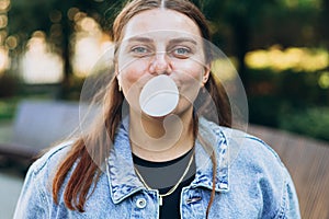 Portrait of young playful hipster female in the park.. Model blowing bubble with chewing gum. Happy 30s Woman looking at